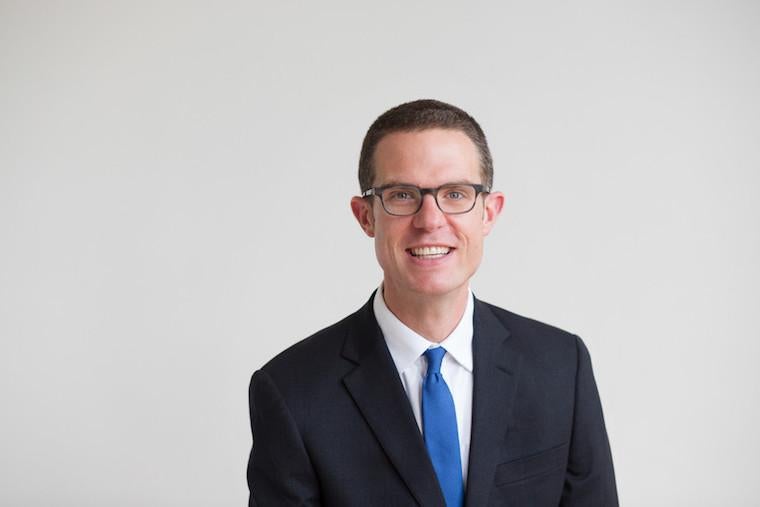 Bill Quillen man in navy suit and blue tie wearing glasses.