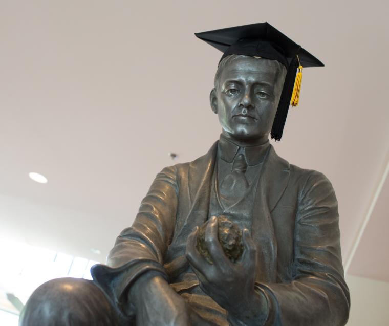 Statue of a man, with a graduation cap placed on its head.
