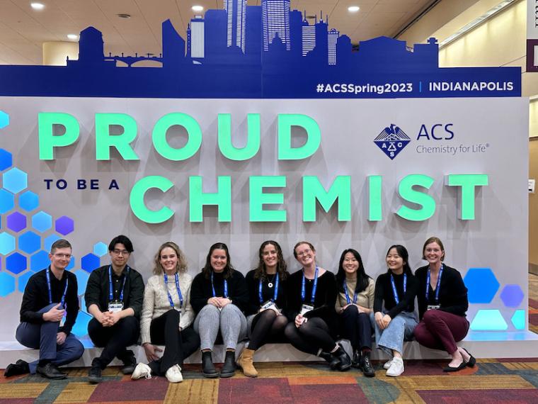 Seven students seated with their mentors in front of a sign that reads "Proud Chemist."