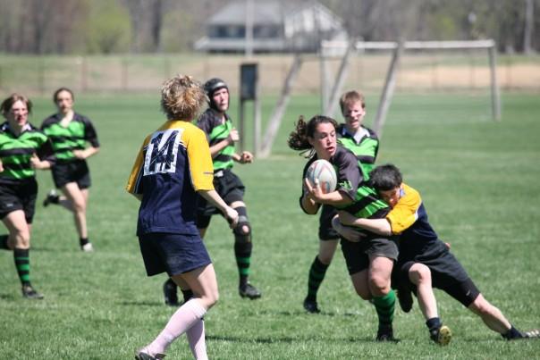 A rugby player with the ball is tackled while other players run toward them.