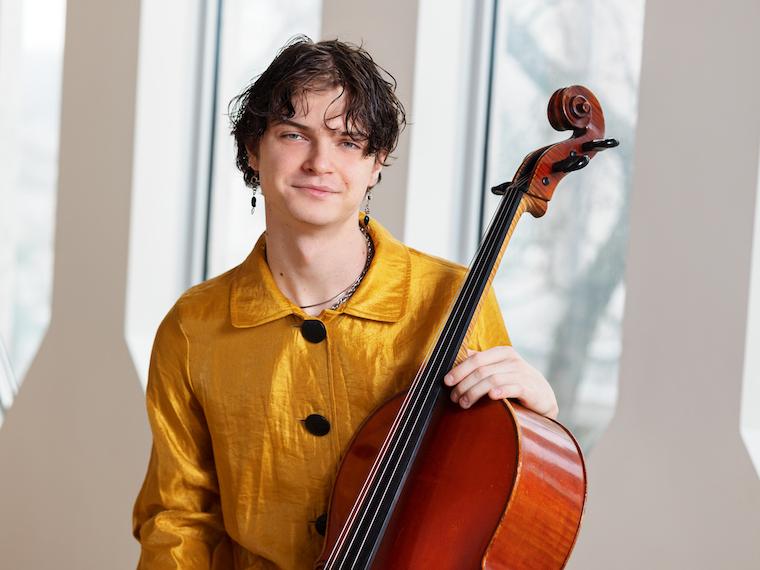 young man in gold shirt, seated with cello