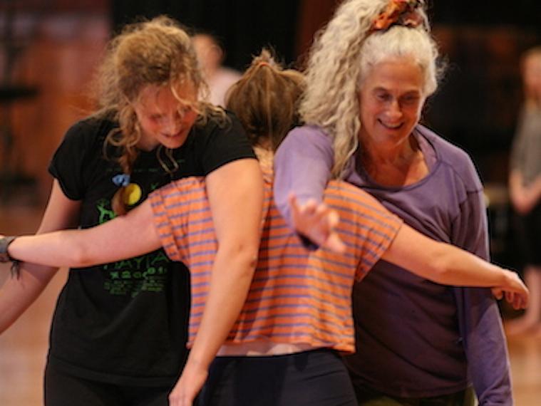 Three contact improv dancers stand together locked arm-in-arm.