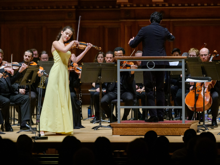 Young woman in yellow dress playing violin accompanied by orchestra