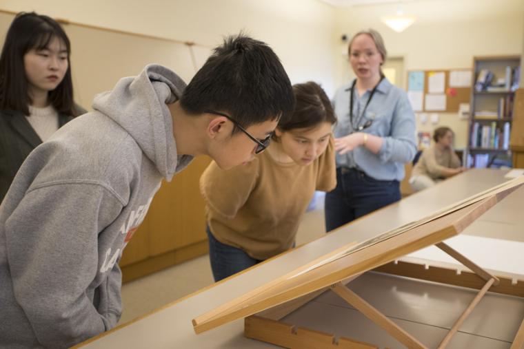 two students bent over looking at a lithograph.