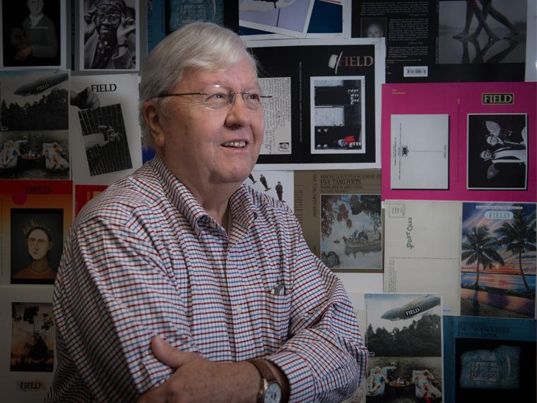 a person wearing a checked shirt smiles in front of a wall with magazine covers