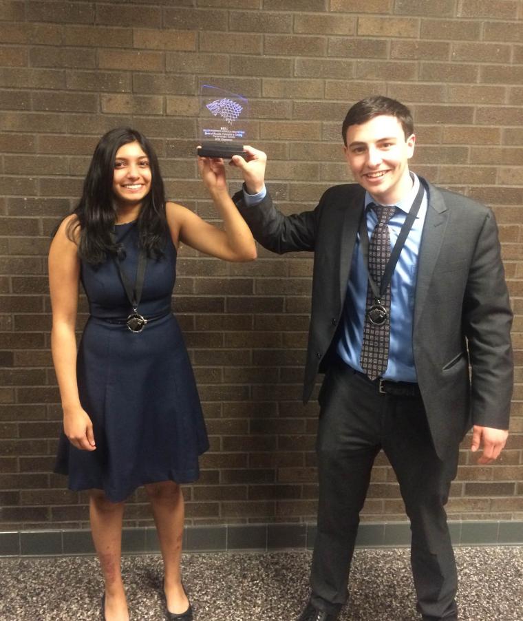 Yasmine and Aaron hold up an award.