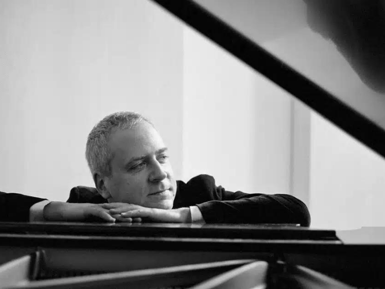 Black and white photo of man sitting arms resting on a piano.
