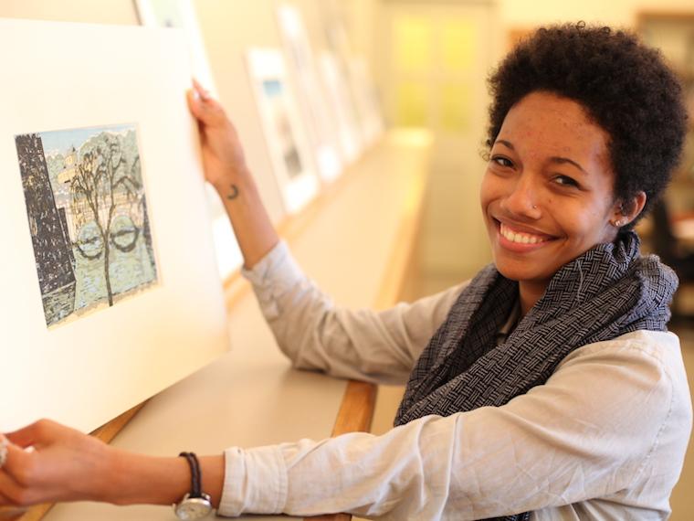 Photograph of a woman holding a piece of artwork and smiling.