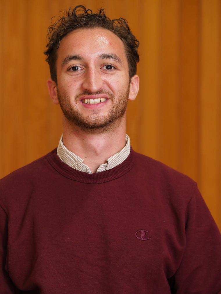 Dylan Mehri standing against a wooden panel.