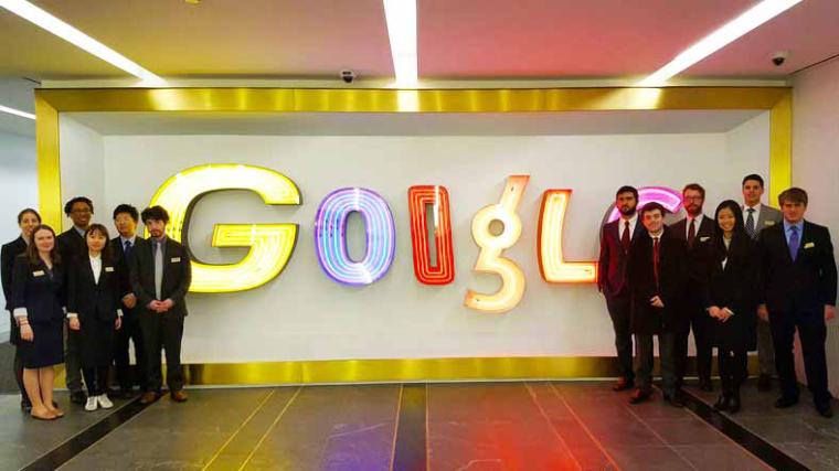 Groups of students stand before an electric Google sign
