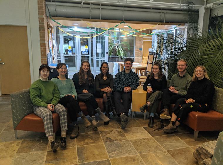 Eight people seated in a row in building lobby.