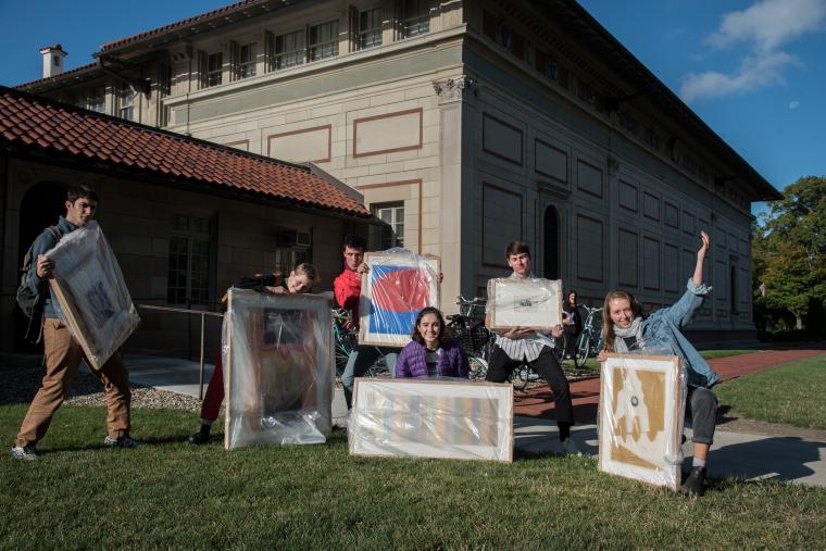 students on lawn holding art work