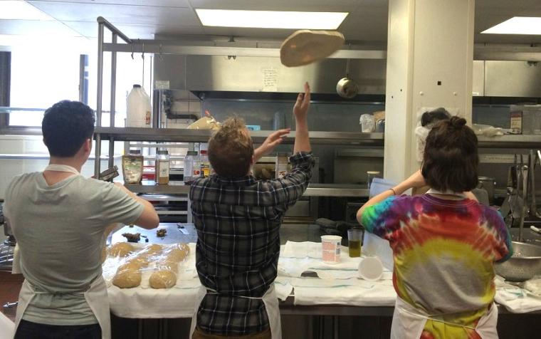 A student cook tosses and spins pizza dough.