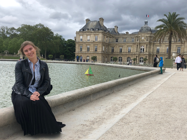 woman sitting in front of a pond and large building in the background.