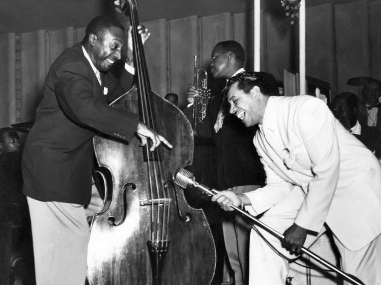 man playing upright bass next to man holding microphone stand.