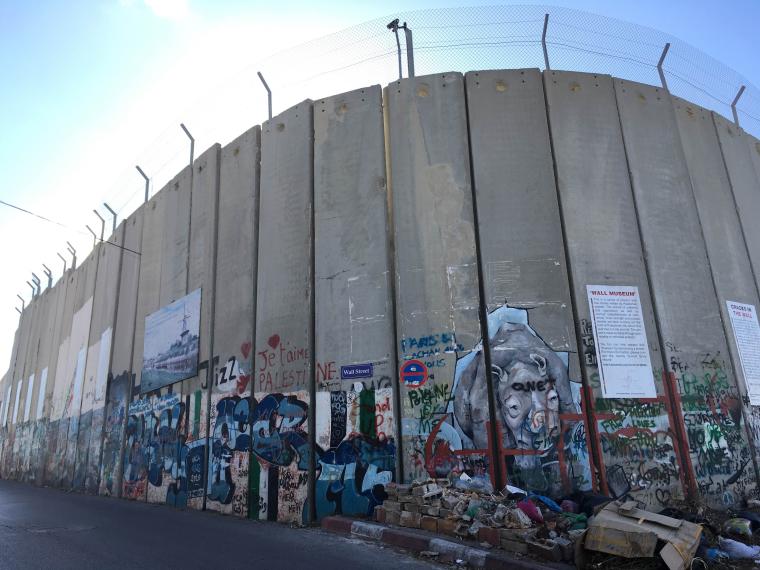 A huge concrete wall is covered in graffiti and topped with barbed wire.