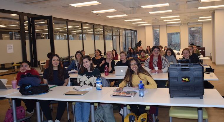 Students sitting at long tables with computers and laptops in a classroom