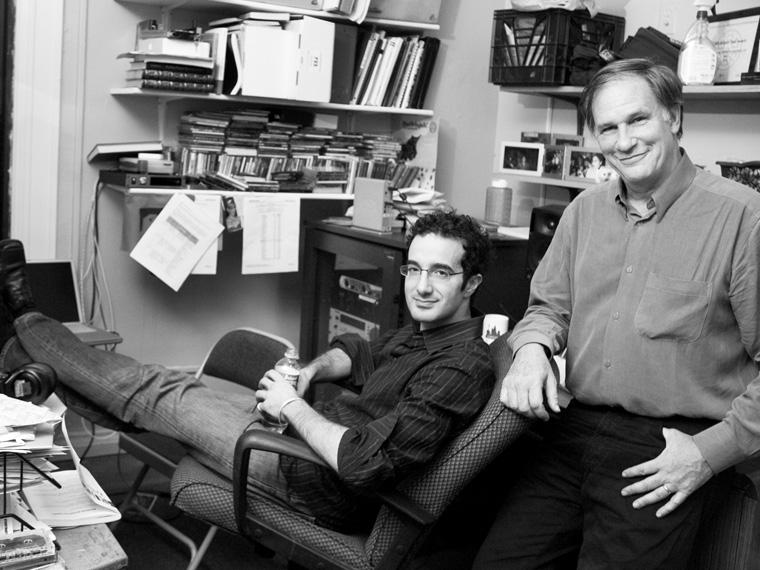 two men sitting in a cozy office full of papers