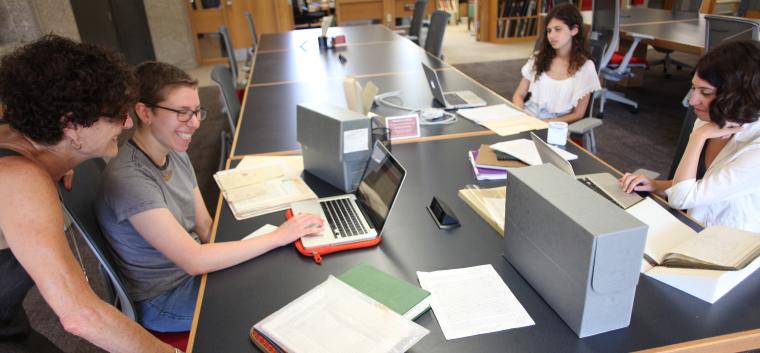 Three students and a professor at a table looking at their laptops