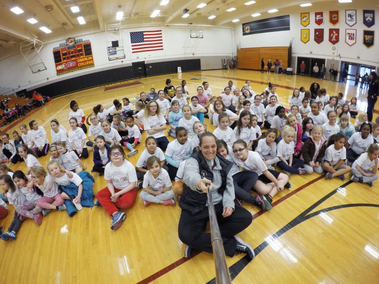 A large group of young girls seated on a gym floor.