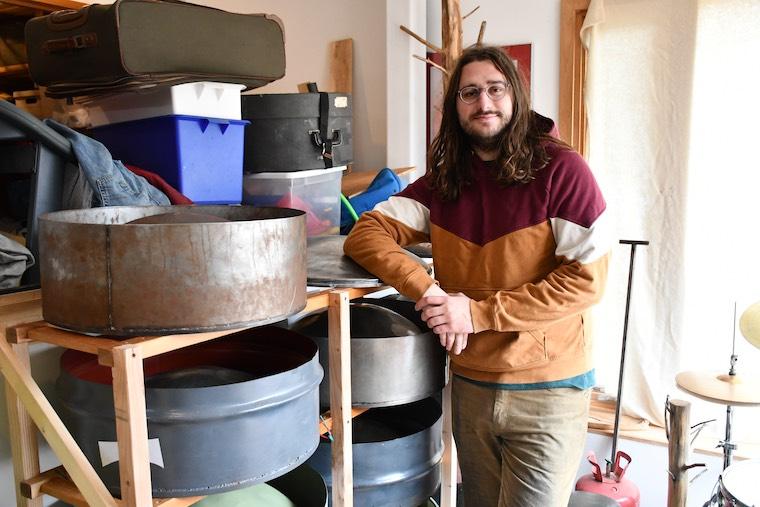 Noah Sanderson leaning against racks filled with steel pan. Photo.