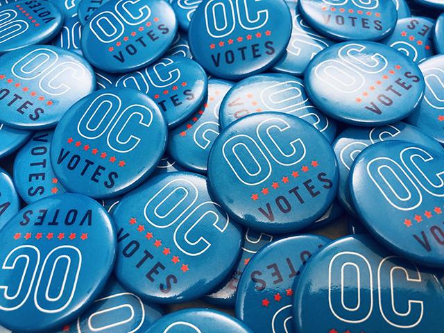 A pile of buttons printed with the OC Votes logo.
