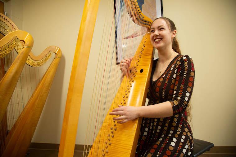 Phoebe Durand-McDonnell smiling and seated playing the harp.