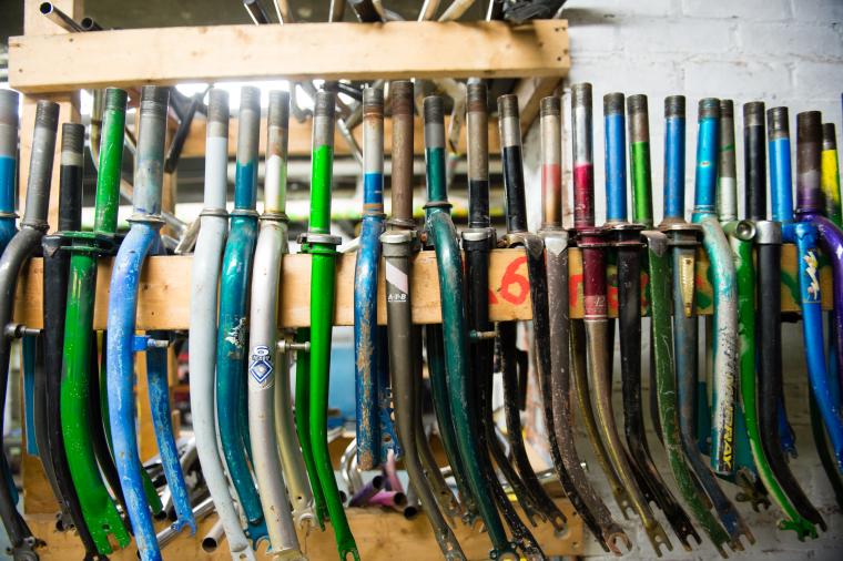 Dozens of used bicycle frame forks are lined up straddling a two-by-four.