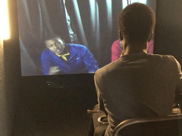 person sitting facing a screen, looking at another person