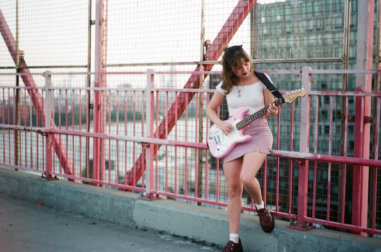 Woman holding a guitar while standing outside in a parking lot.