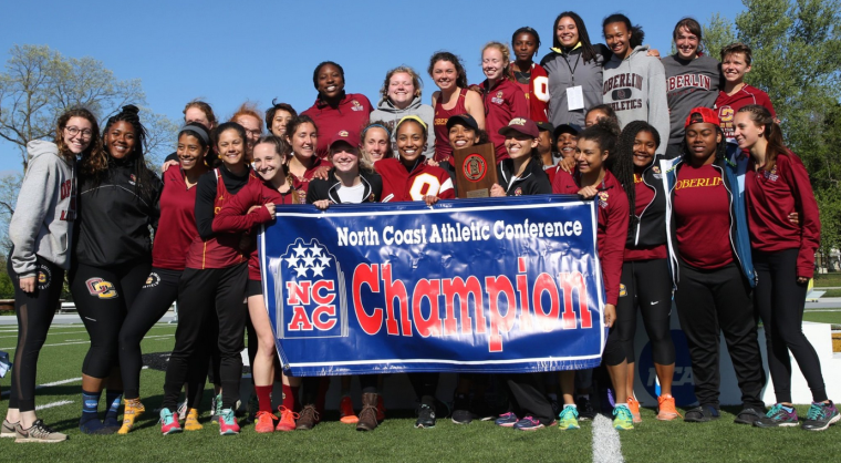 A group of about 2 dozen women pose on an athletic field. They are holding a banner that says 'North Coast Athletic Conference Champions'.