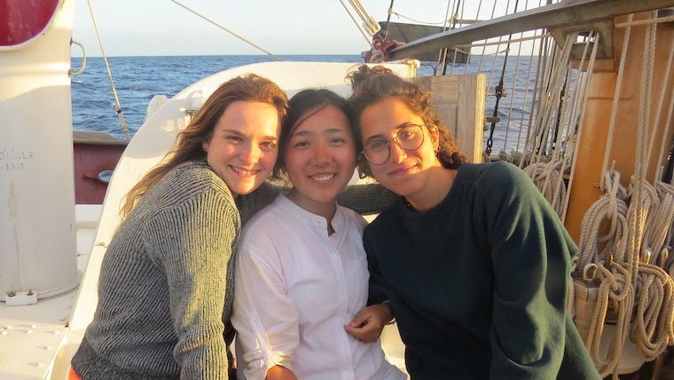 Three people leaning against each other, smiling on a boat. Photo.
