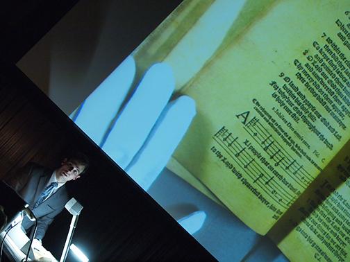 A gloved hand touches the page of an old book.