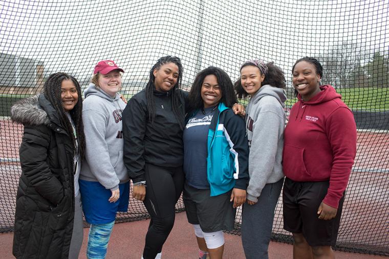 Six women posing by an athletics track
