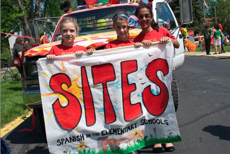 3 school-age girls hold a sign that reads SITES Spanish in the Elementary Schools