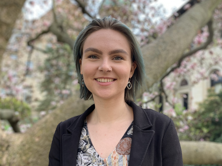 woman in v-neck smiling with tree blossoms in background.