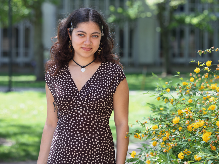 Student fellowship award winner smiles as they stand on campus green with iconic buildings in the background.