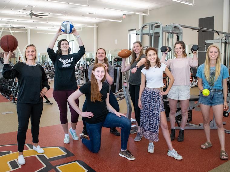 Photo of eight members of the Stronger Together group posing with sports equipment in the gym