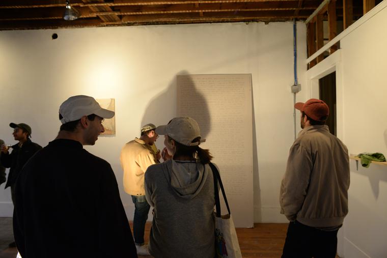 Gallery visitors look at art on the walls of a roughly finished room