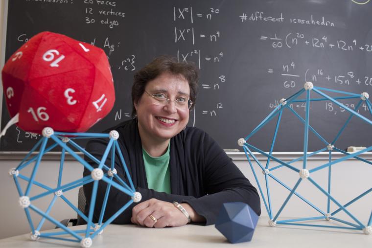 Professor Colley with geometric models on her desk. The blackboard behind her is filled with equations.