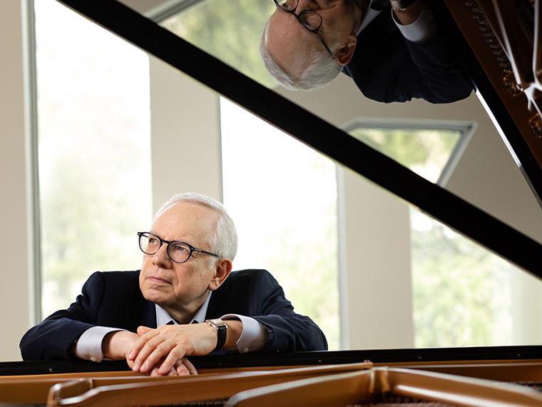 man with glasses wearing a dark suite sits at the piano