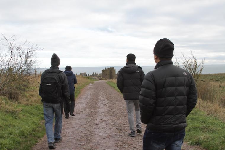 Four students in winter coats walk toward a castle.