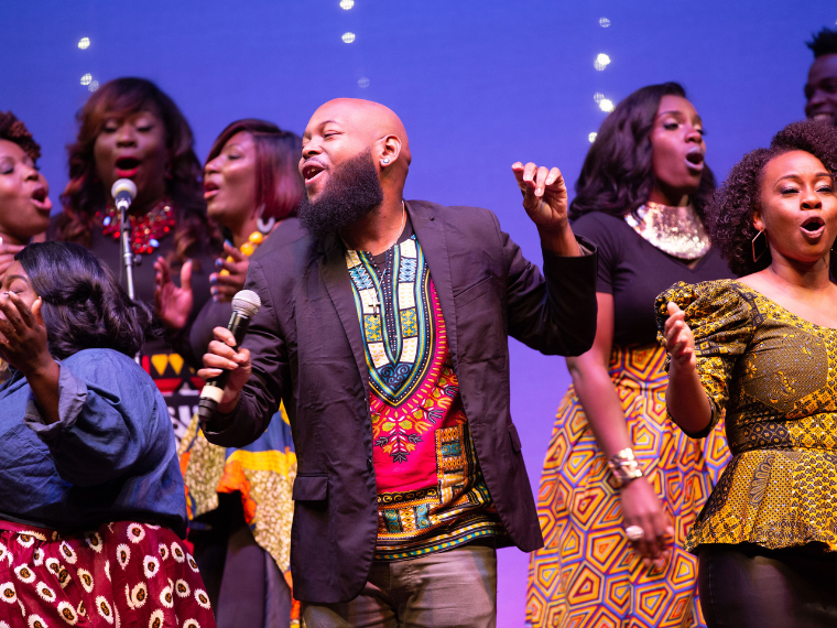 Men and women onstage wearing brightly colored clothes and singing