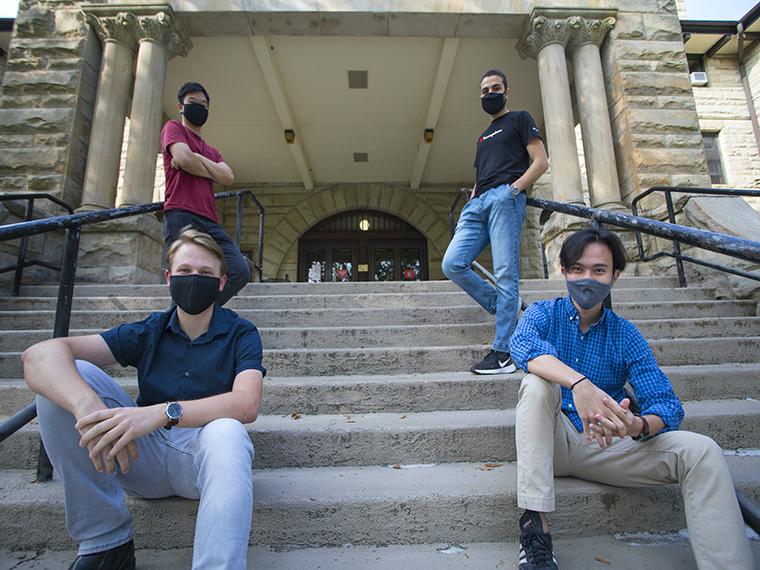 Four people wearing face coverings sit on stone steps.