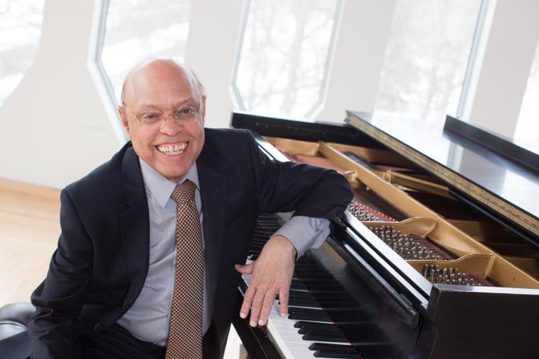 Naboré is seated at a grand piano, with the distinctive windows of Bibbins Hall in the background