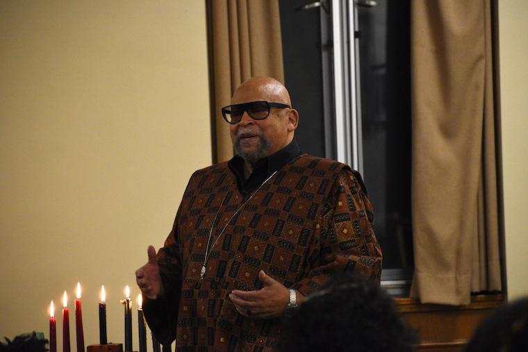 Man in African attire standing behind a table with a candle holder of 9 lit candles.