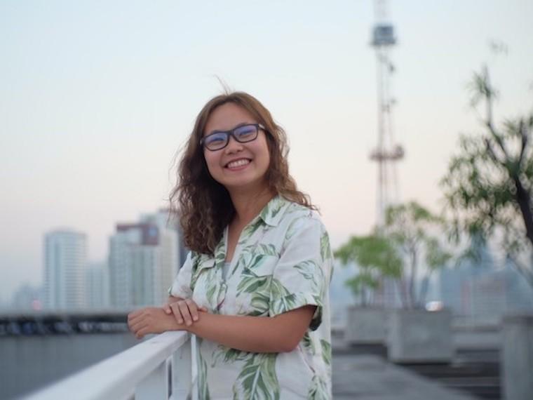 young woman outside standing alongside a railing overlooking a lake