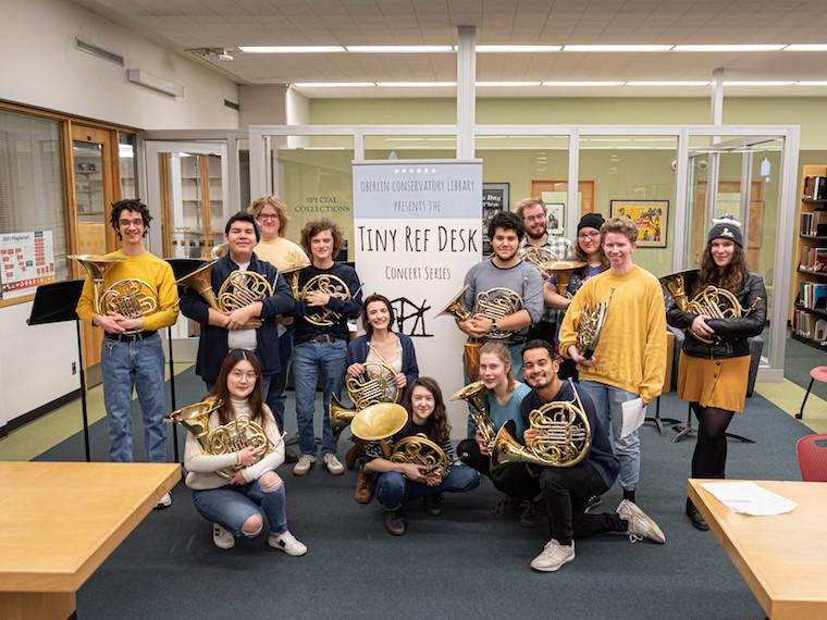 Students with French horns pose in front of a sign.