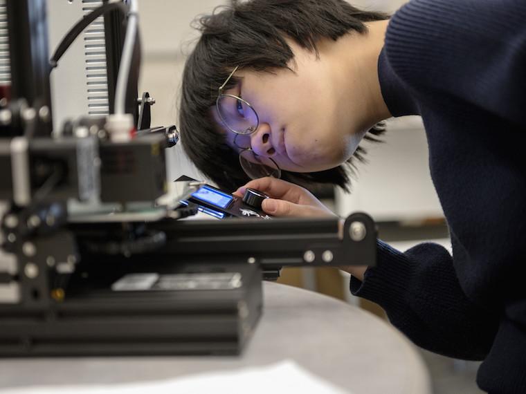 A student looks closely at a plat on a printer.