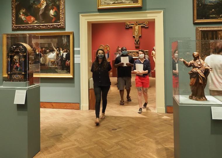 People wearing mouth and nose masks walk through an art gallery.